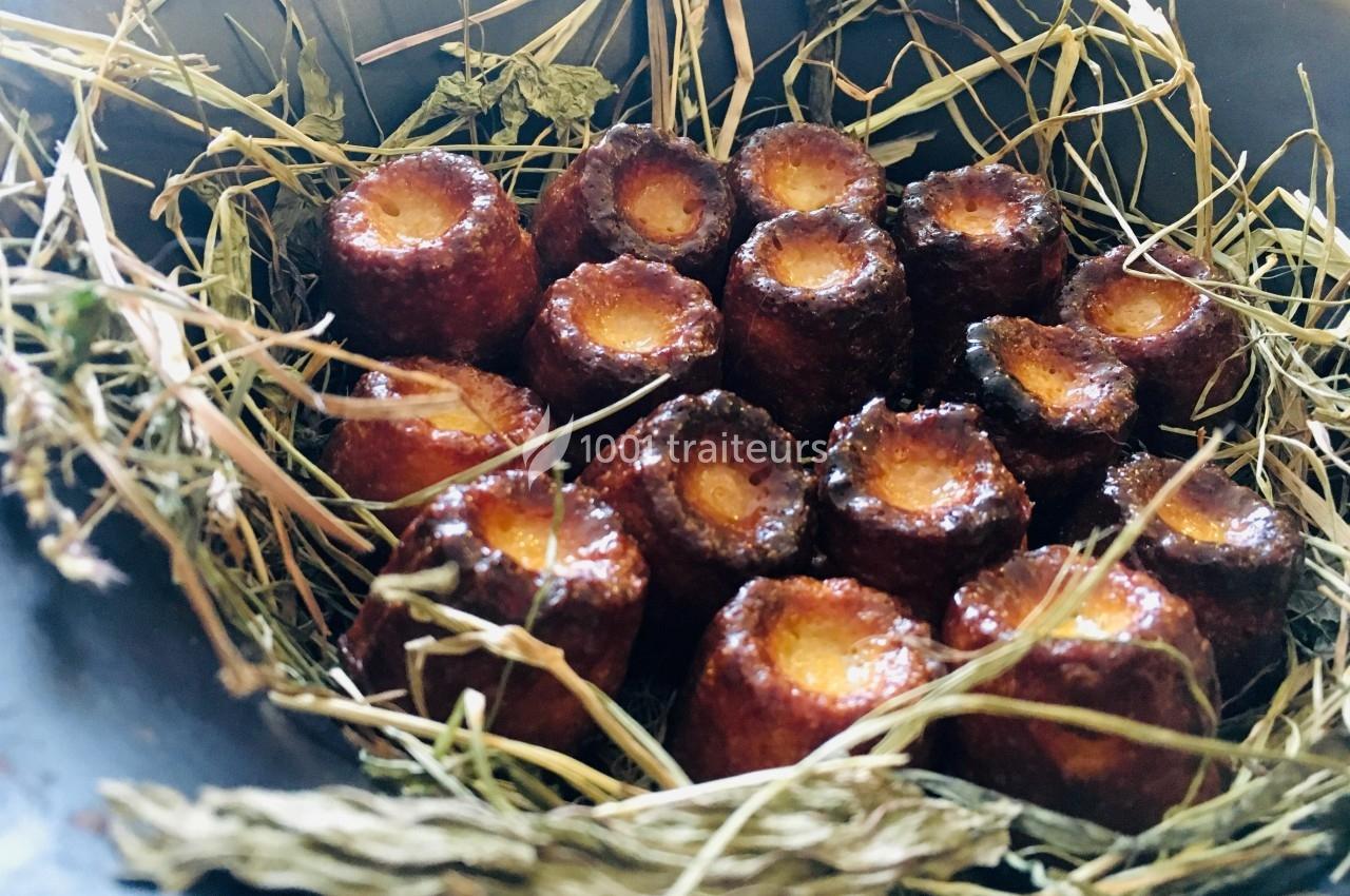 Cannelés dorés disposés sur un lit de paille dans un récipient sombre.