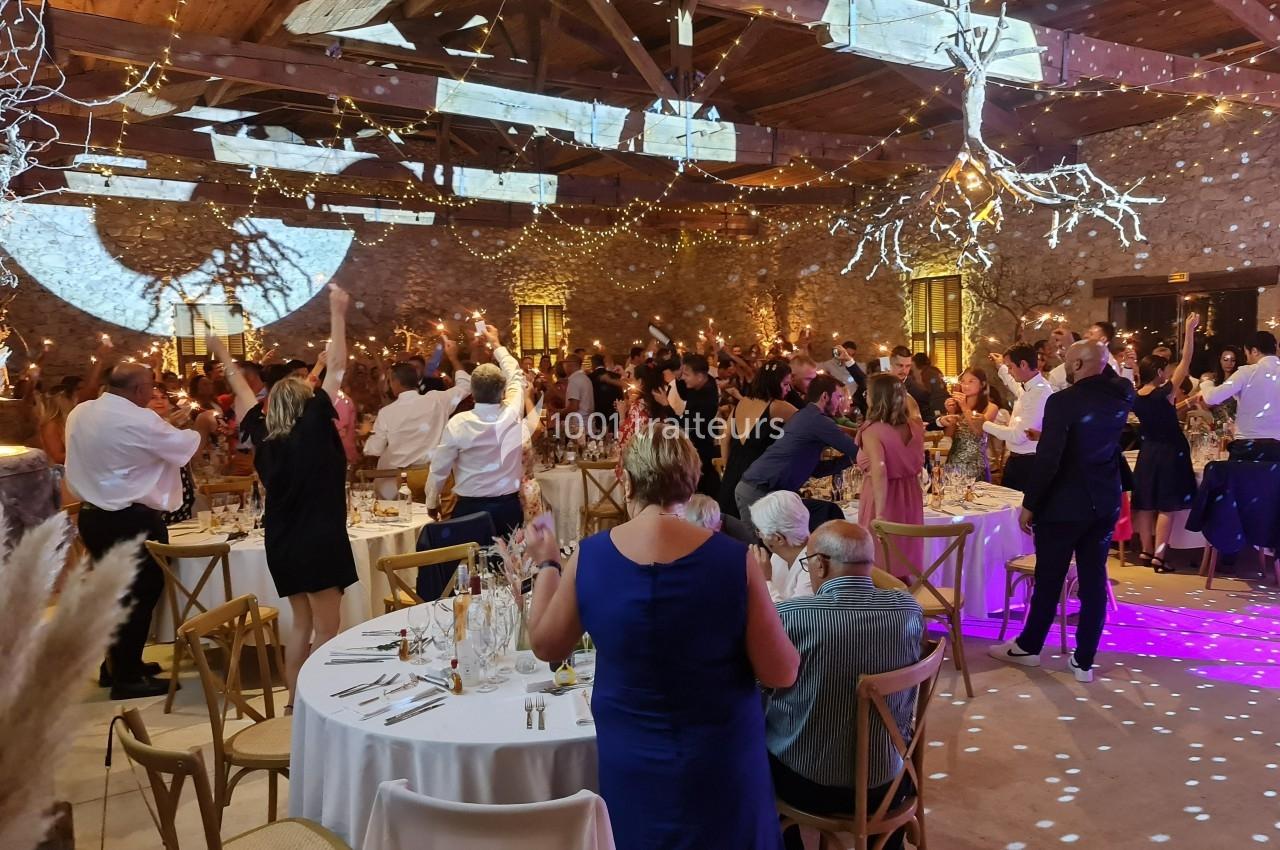 Salle de réception décorée avec des guirlandes lumineuses, des invités dansant et des tables dressées pour un événement…