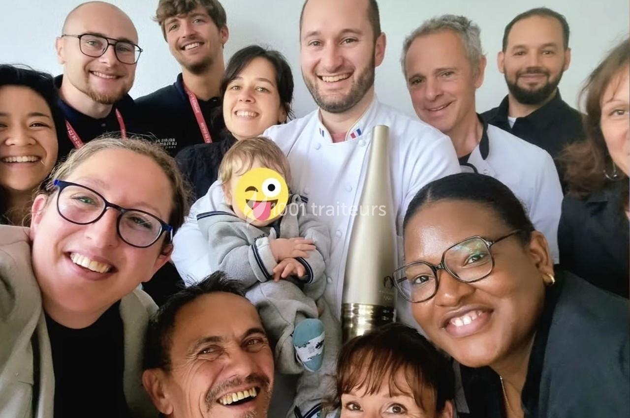 Un groupe de personnes souriantes posant ensemble, dont un chef en tenue blanche tenant un trophée et un enfant.