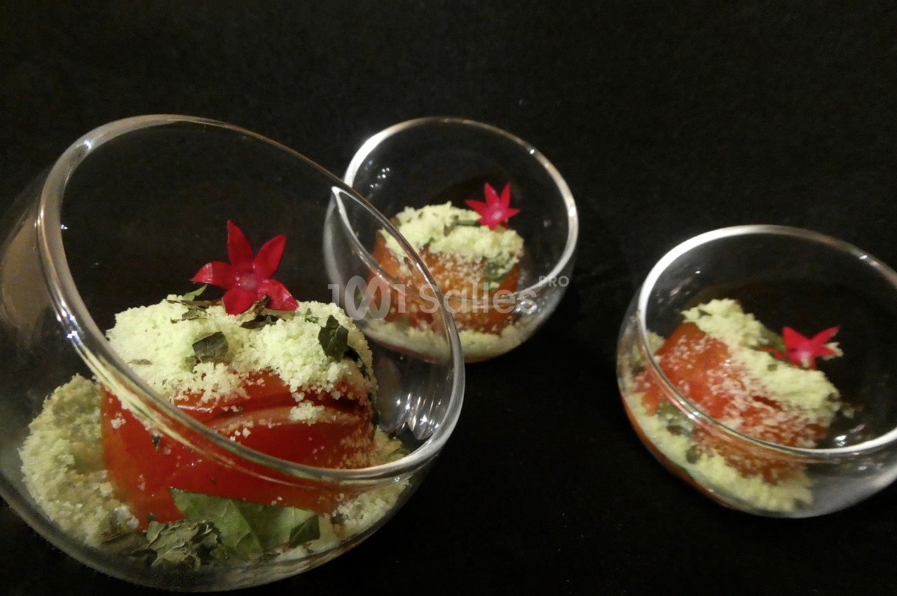 Trois verrines contenant une préparation à base de tomate, herbes fraîches, poudre verte et fleurs rouges décoratives.