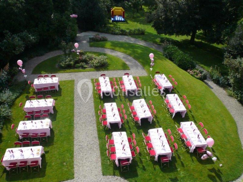Tables dressées avec nappes blanches et chaises rouges disposées dans un jardin pour un événement en plein air.