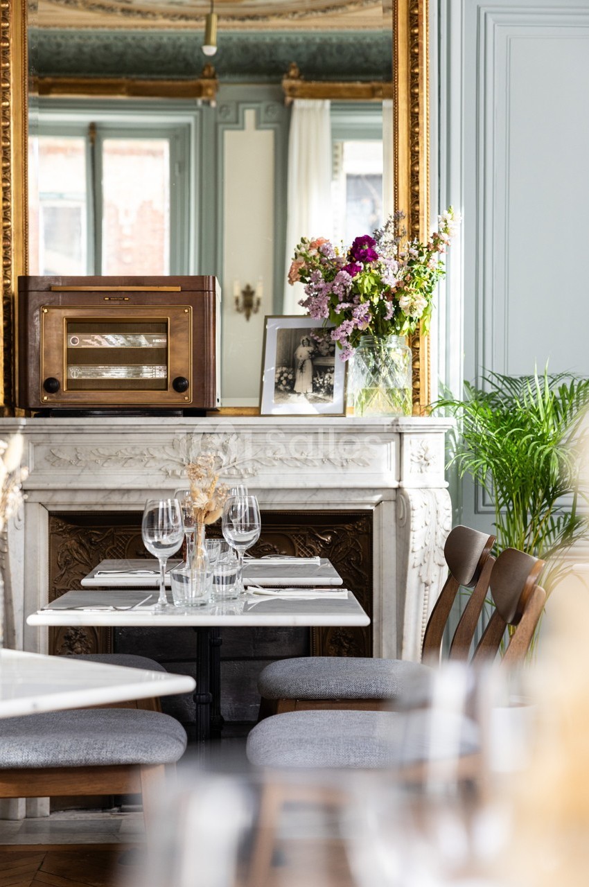 Table dressée devant une cheminée en marbre ornée d'un miroir doré, avec un bouquet de fleurs et une radio vintage.