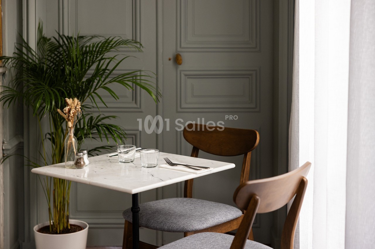 Table en marbre blanc avec deux chaises en bois, près d'une plante verte et d'une porte grise.