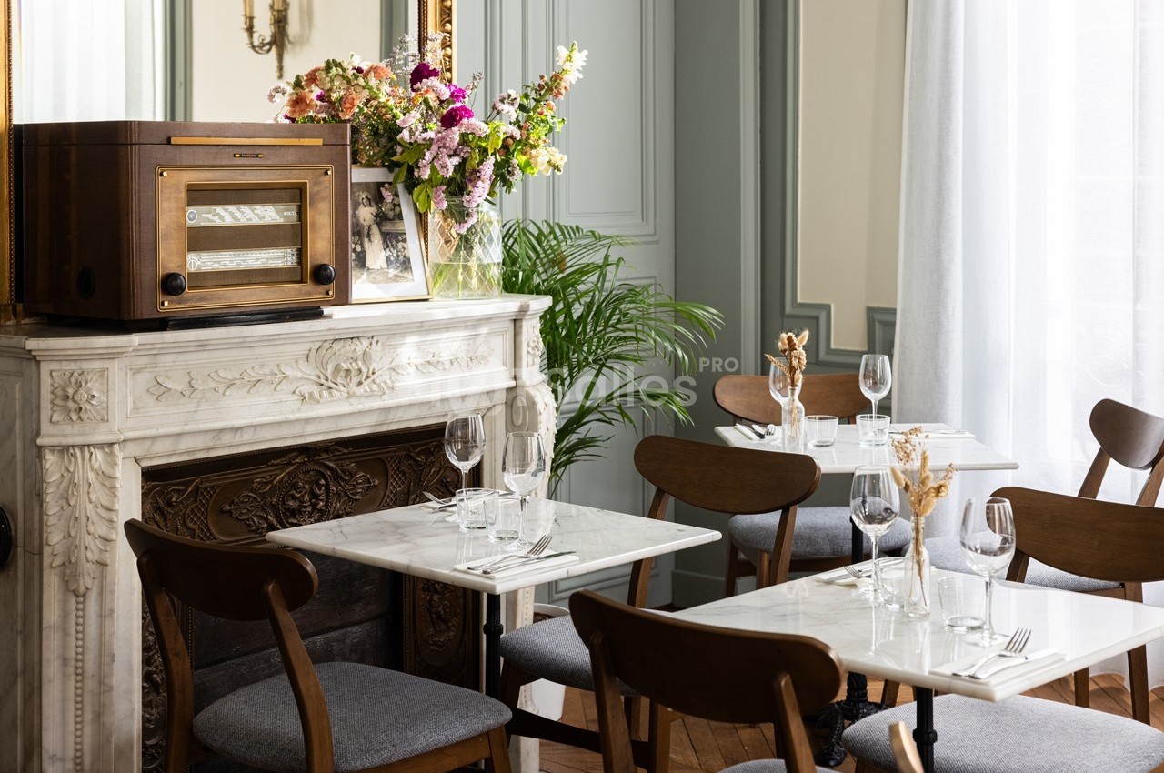 Salle de restaurant élégante avec tables en marbre, chaises en bois, cheminée décorative et bouquet de fleurs colorées.