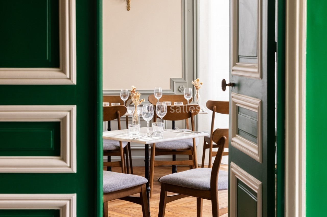 Salle à manger élégante avec table dressée, chaises en bois et lumière naturelle entrant par une fenêtre.