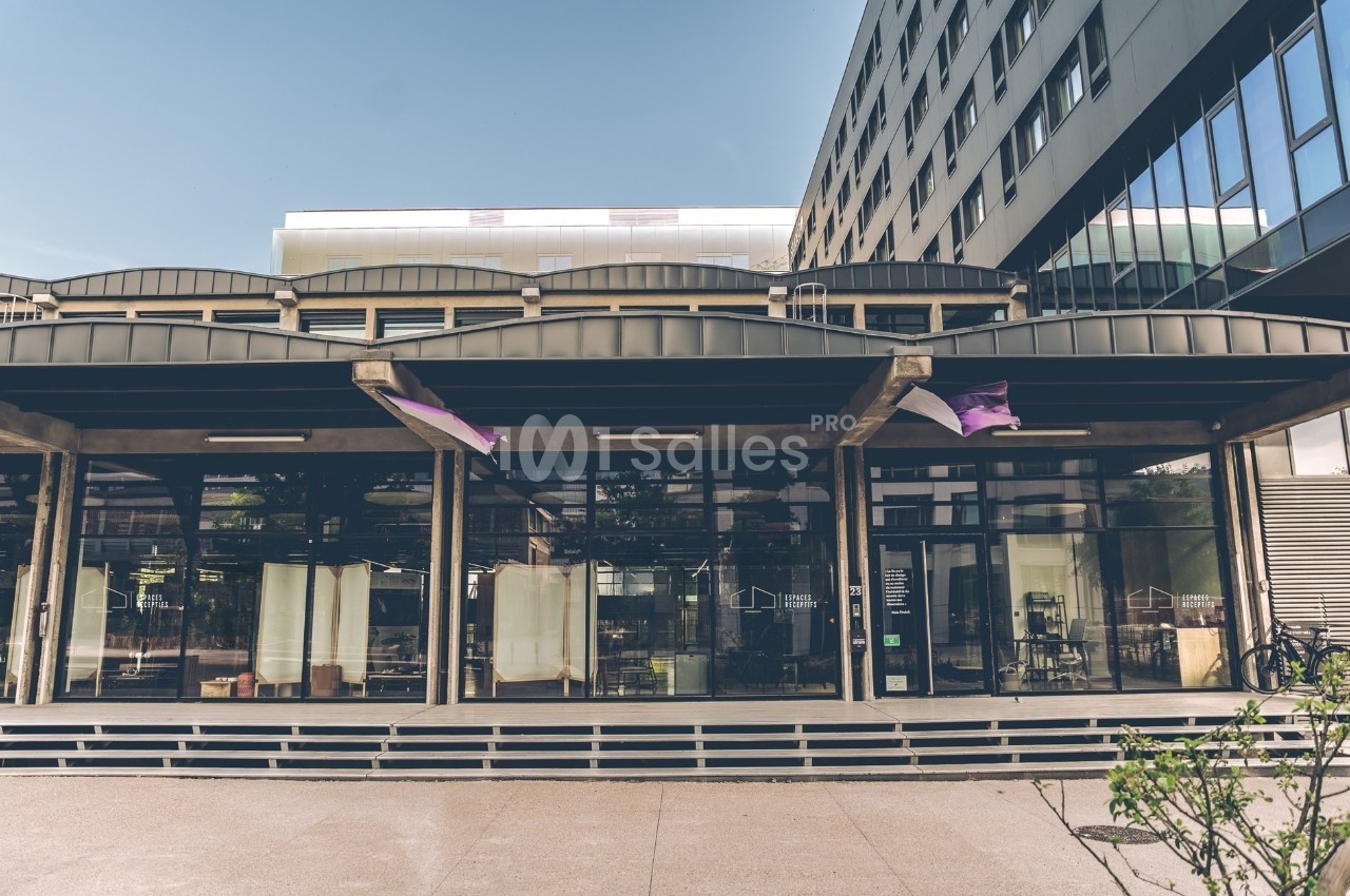 Façade vitrée d'un bâtiment moderne avec des drapeaux suspendus et une entrée visible au rez-de-chaussée.