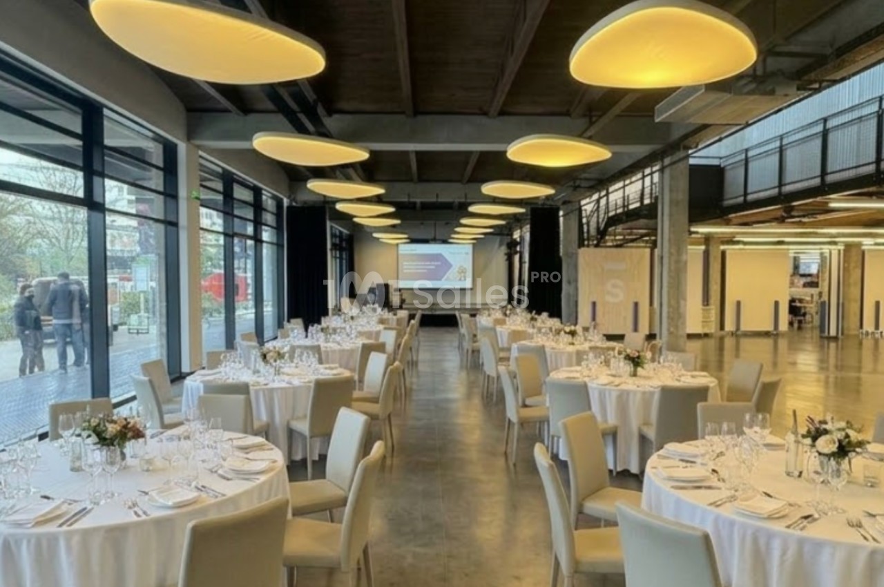 Salle de réception moderne avec tables rondes dressées, grandes baies vitrées et éclairage suspendu.