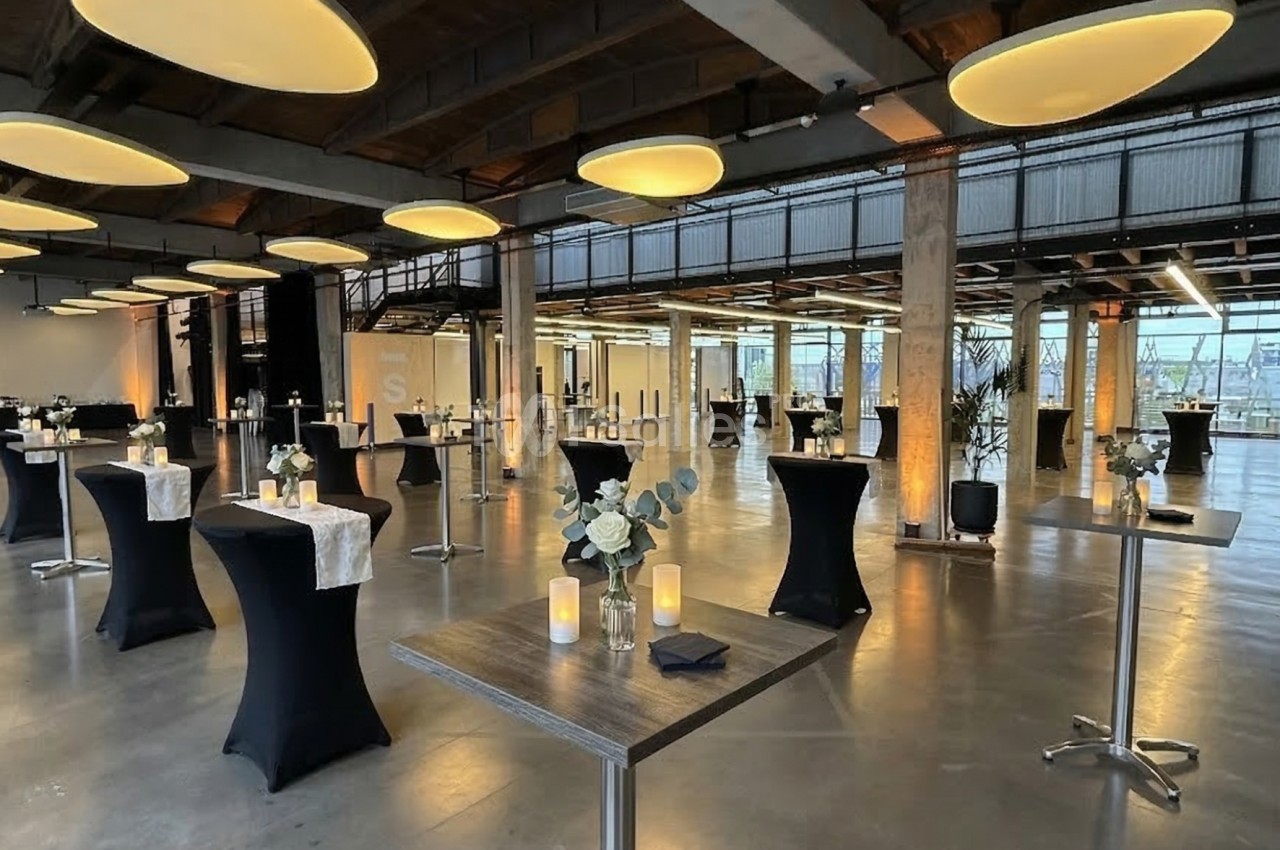 Salle moderne aménagée pour un événement, avec tables hautes décorées, bougies et éclairage chaleureux.