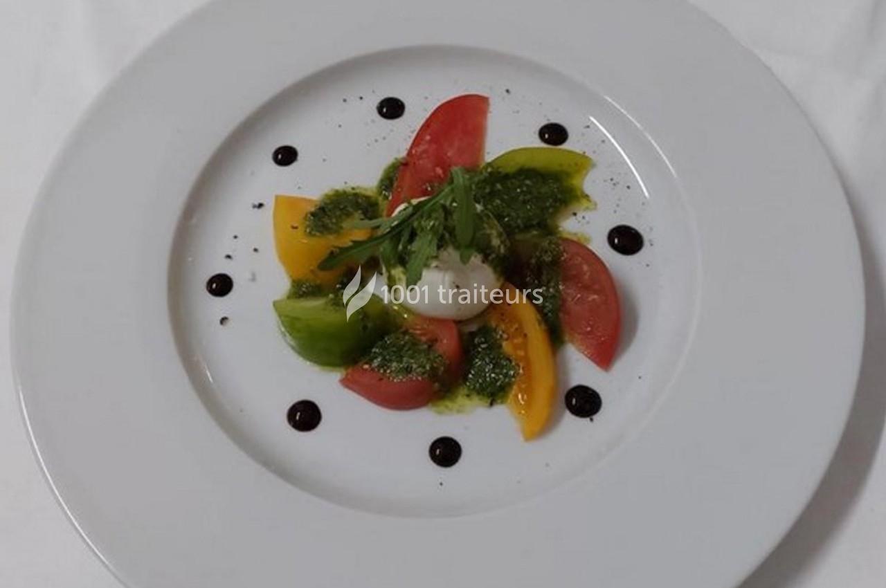 Assiette de salade colorée avec tomates, burrata, pesto, roquette et points de vinaigre balsamique.