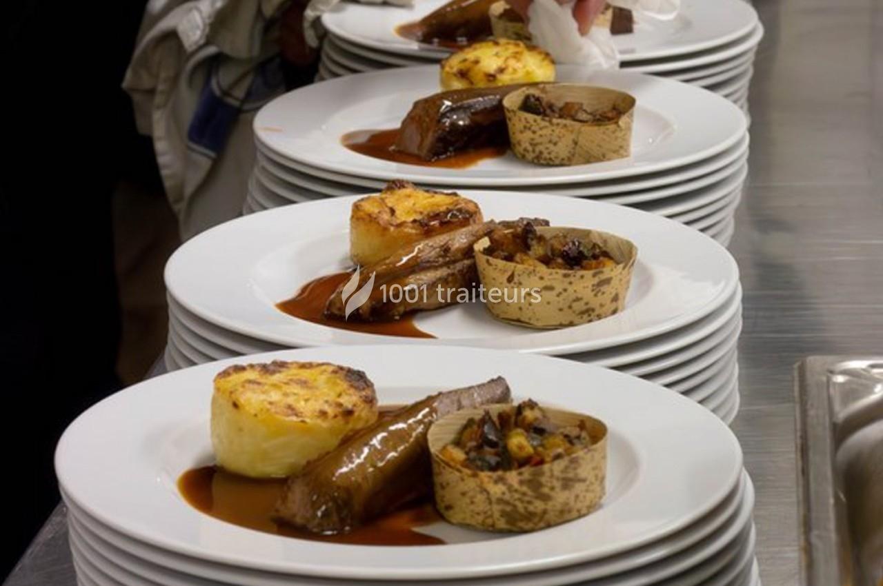 Assiettes dressées avec viande, gratin, garnitures et sauce, alignées sur un plan de travail en cuisine.