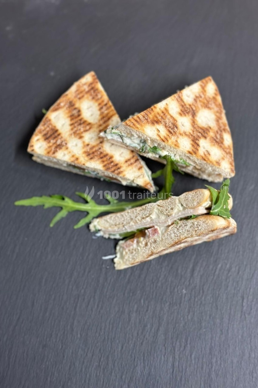 Triangles de sandwichs grillés garnis de roquette et d'ingrédients visibles sur une ardoise noire.