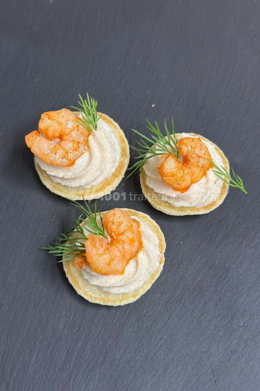 Canapés sur crackers garnis de crème, crevettes assaisonnées et brins d'aneth, présentés sur une ardoise noire.