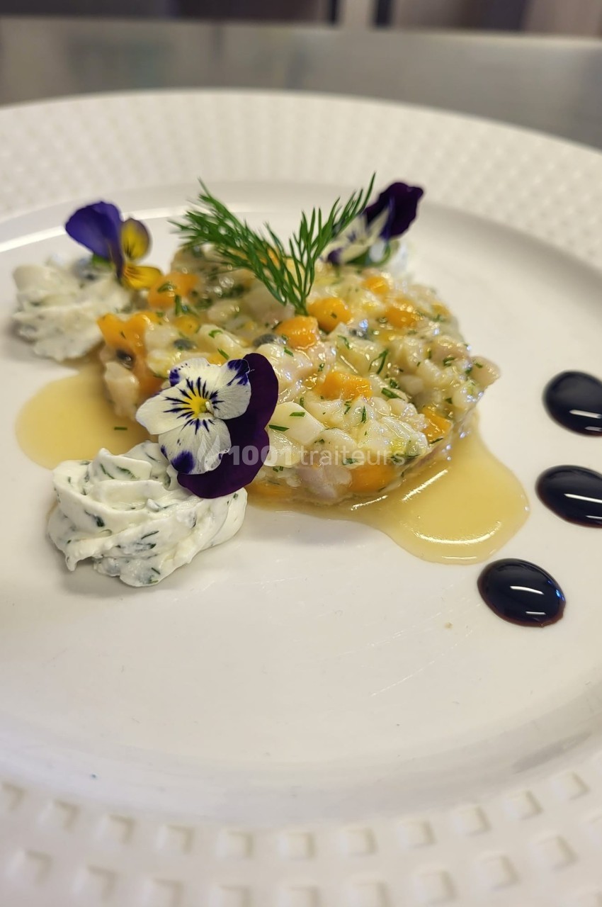 Assiette de tartare de poisson décorée de fleurs comestibles, sauce, crème aux herbes et gouttes de réduction balsamique.