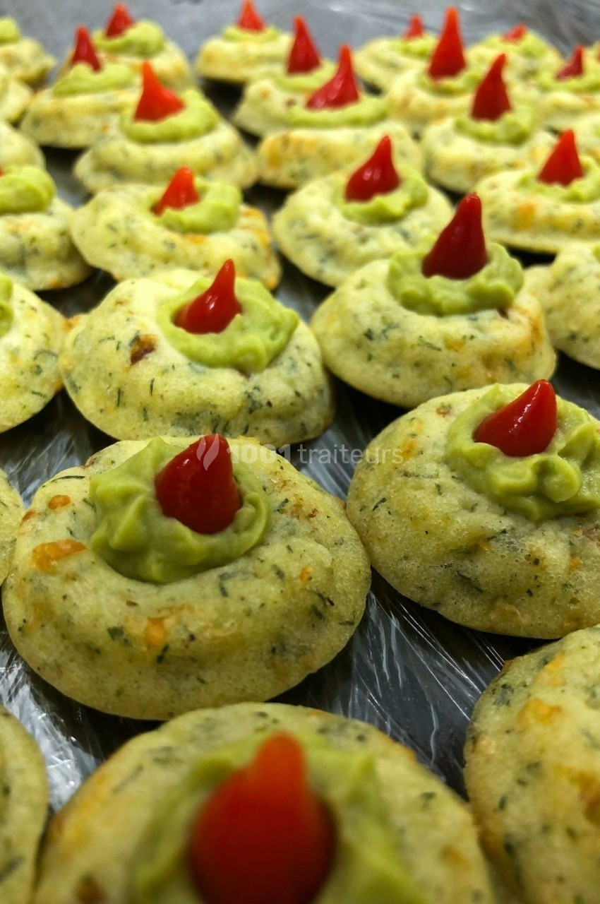 Biscuits salés garnis de crème verte et décorés de petits morceaux rouges en forme de pointe.