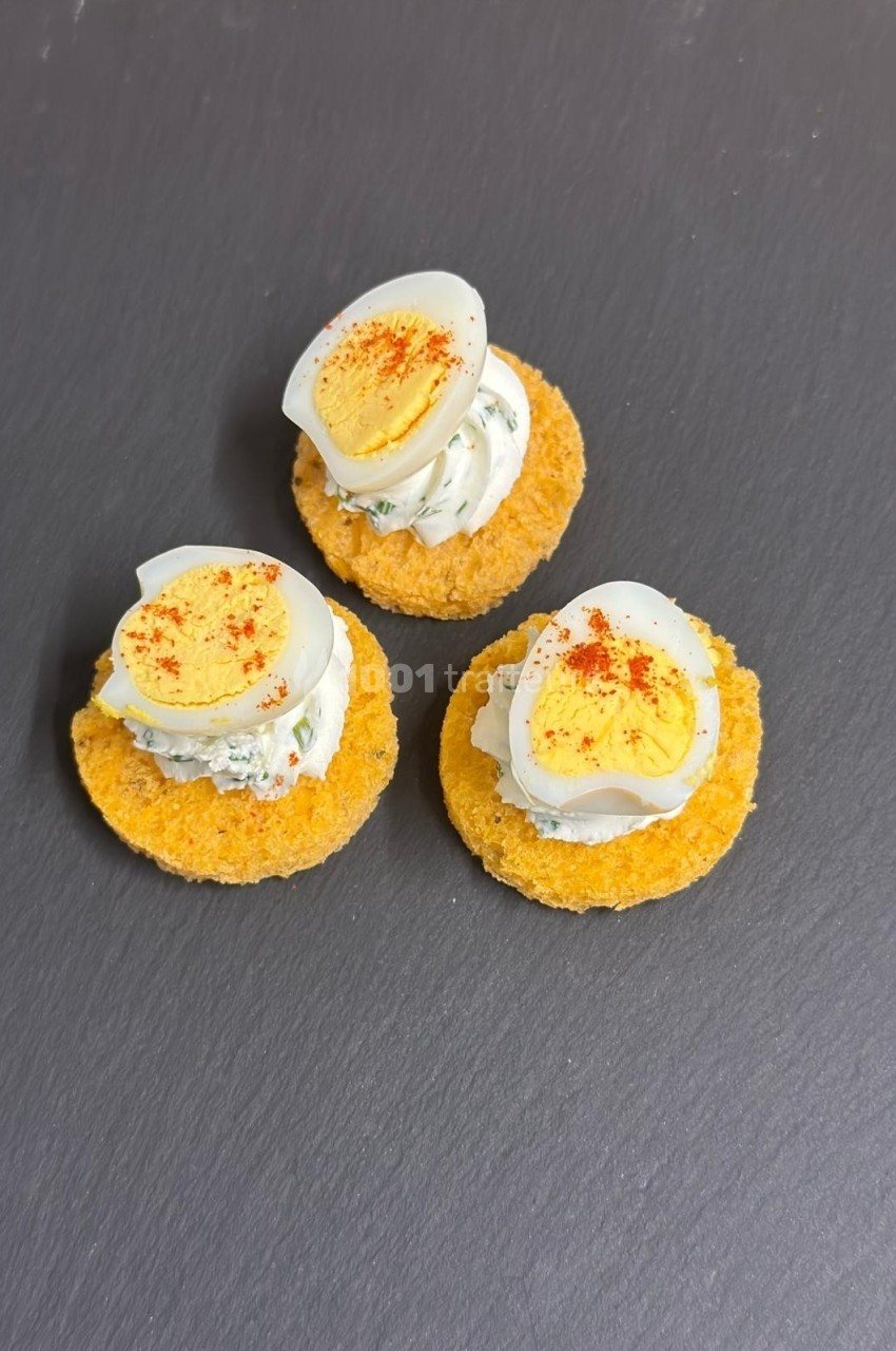Trio de canapés sur ardoise, garnis de crème aux herbes, rondelles d'œuf dur et une pincée de paprika.