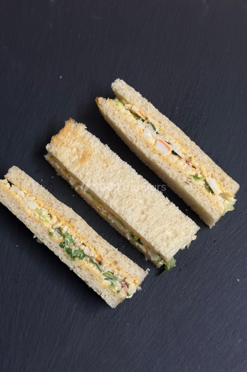 Trois sandwichs triangulaires garnis de légumes et de sauce, présentés sur une surface noire.