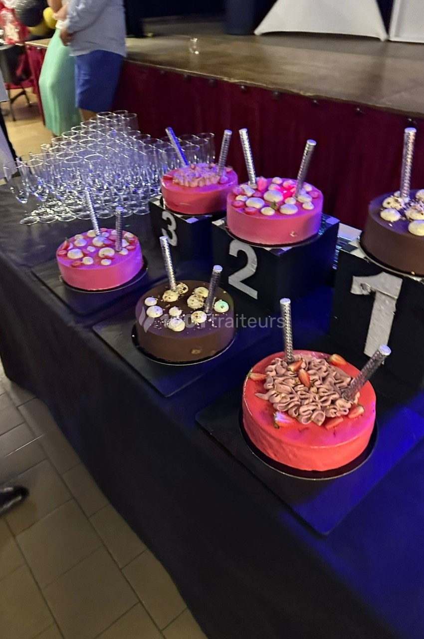 Gâteaux numérotés sur une table noire, décorés de bougies et de garnitures, avec des verres empilés en arrière-plan.