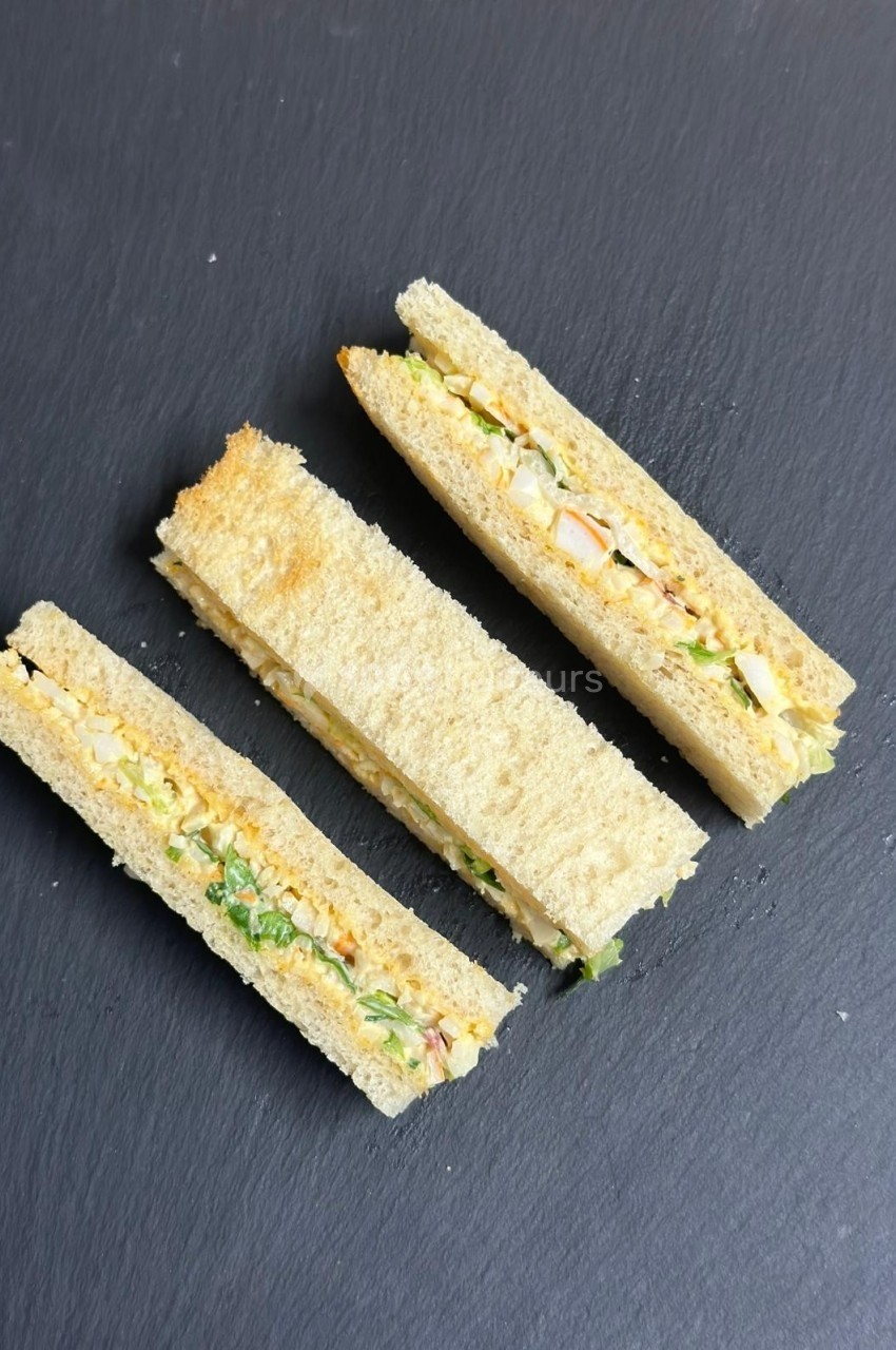 Trois sandwichs triangulaires garnis de légumes et de sauce, disposés sur une ardoise noire.