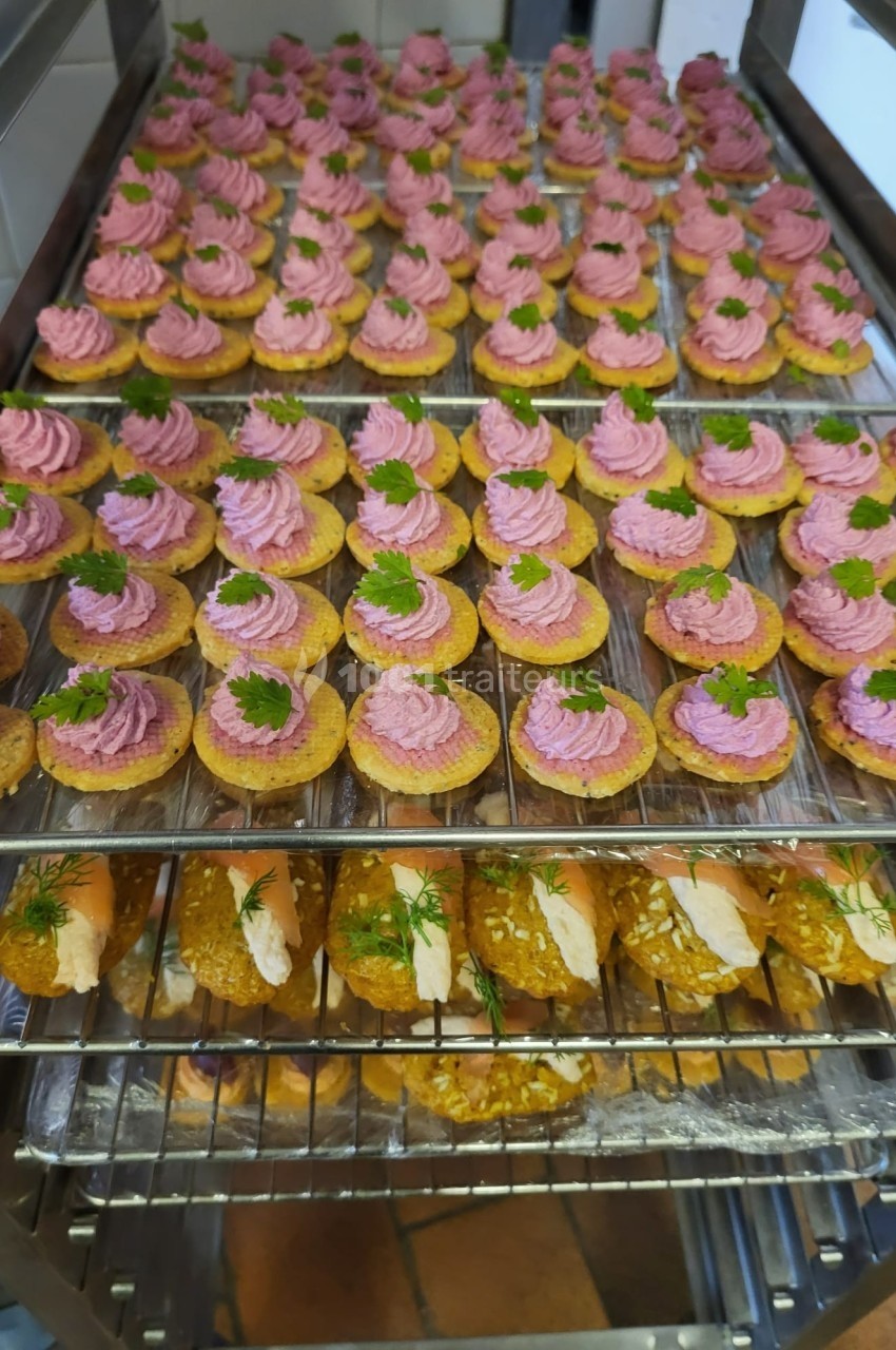 Plateaux garnis de bouchées apéritives, dont des toasts à la mousse rose et des roulés garnis, disposés sur des grilles.