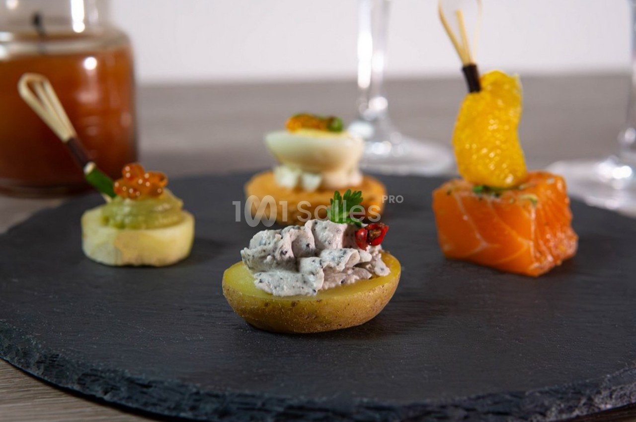 Assortiment de bouchées apéritives sur une ardoise, comprenant poisson, œuf, mousse et garnitures variées.