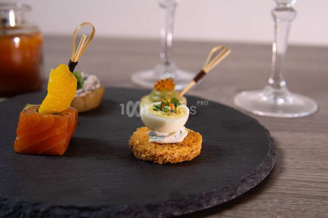 Assortiment de bouchées apéritives sur une ardoise, comprenant saumon, œuf farci et garnitures variées.