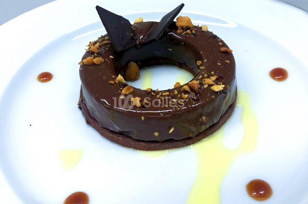 Dessert en forme d'anneau avec glaçage au chocolat, éclats de noisettes, décoration en chocolat et sauce autour.
