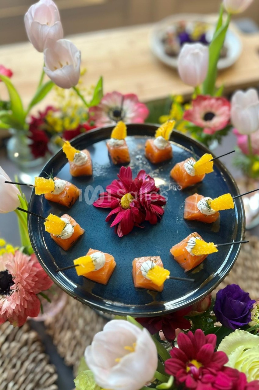Plateau de bouchées de saumon avec décoration florale colorée en arrière-plan.