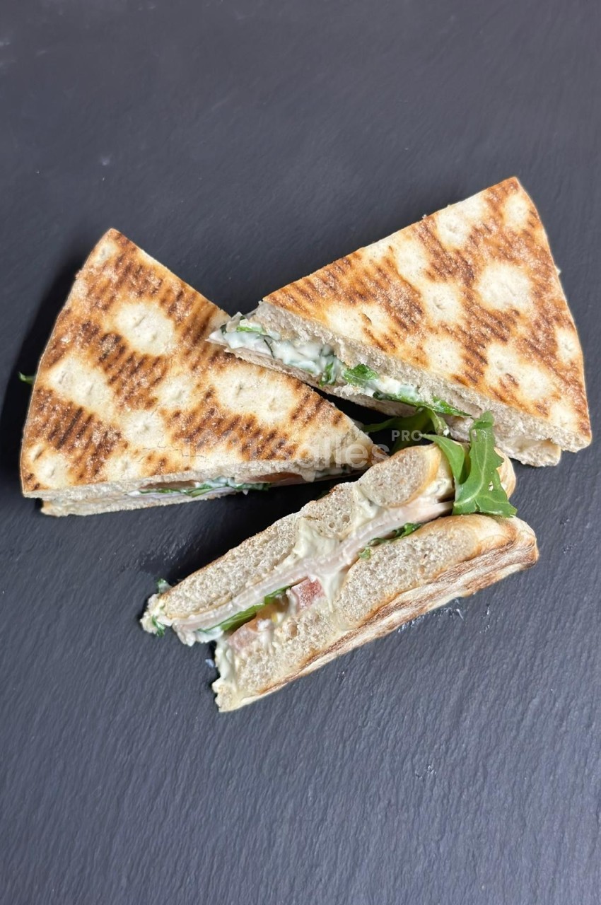 Triangles de sandwich grillé garnis de roquette, fromage et jambon, présentés sur une surface noire.