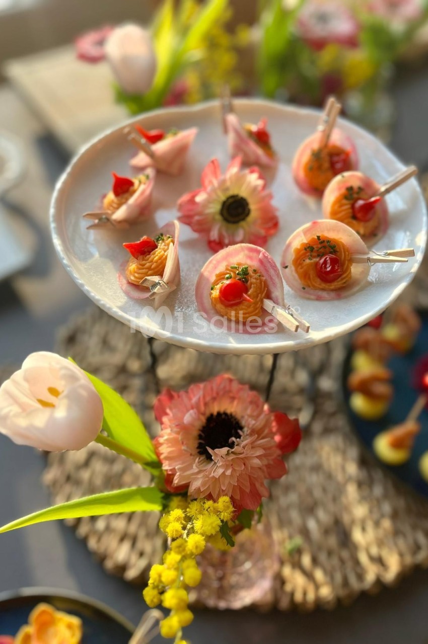 Plateau de bouchées apéritives colorées sur un présentoir, entouré de fleurs décoratives.