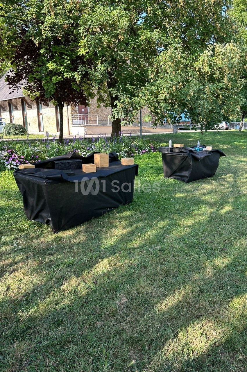 Deux tables recouvertes de nappes noires avec des objets en bois et des accessoires, installées dans un parc verdoyant.