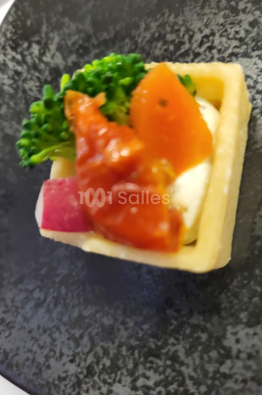 Tartelette garnie de légumes colorés, brocoli, tomate et fromage, présentée sur une assiette noire.