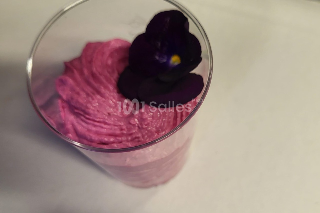 Mousse rose servie dans un verre transparent, décorée d'une fleur violette comestible.