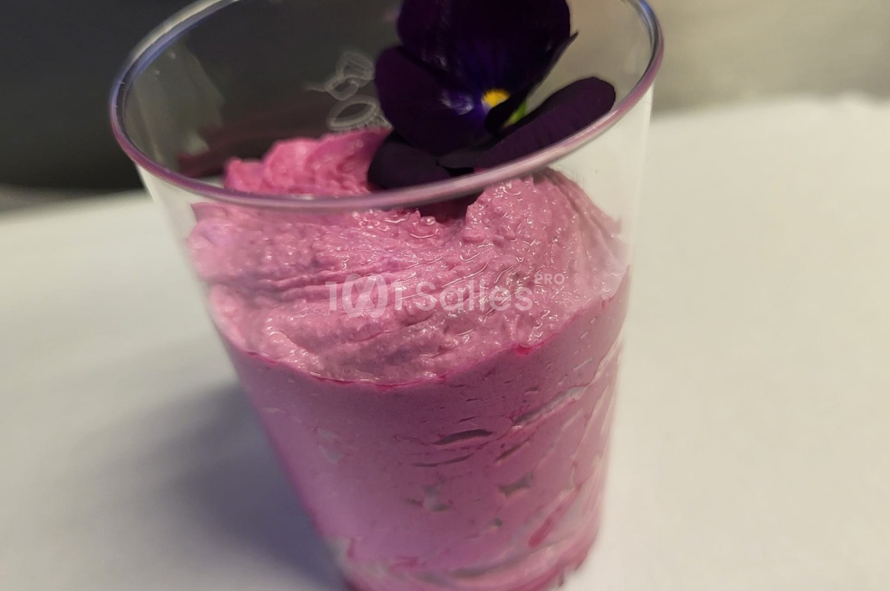 Mousse rose servie dans un verre transparent, décorée d'une fleur violette comestible.