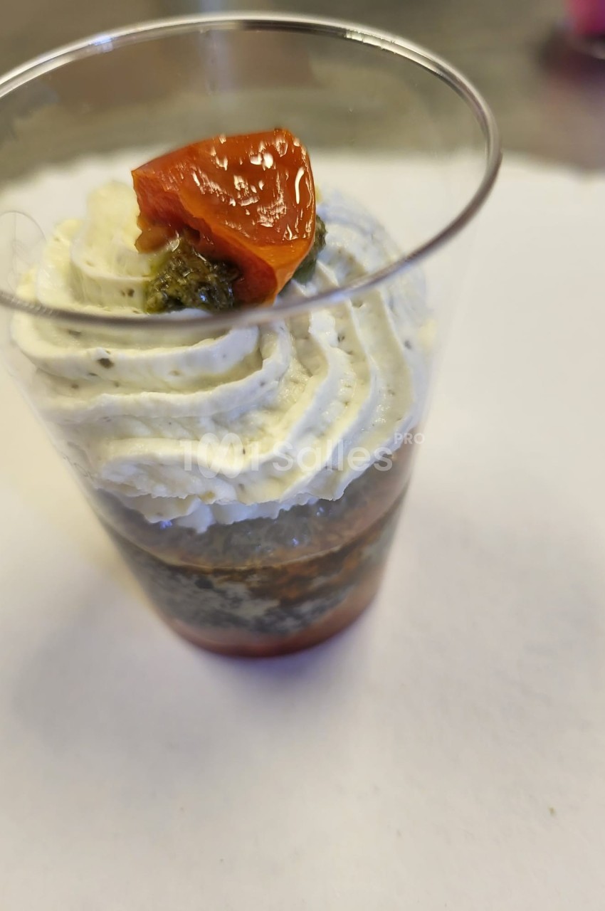 Verrine garnie de couches de crème, tapenade et tomate confite sur un fond blanc.