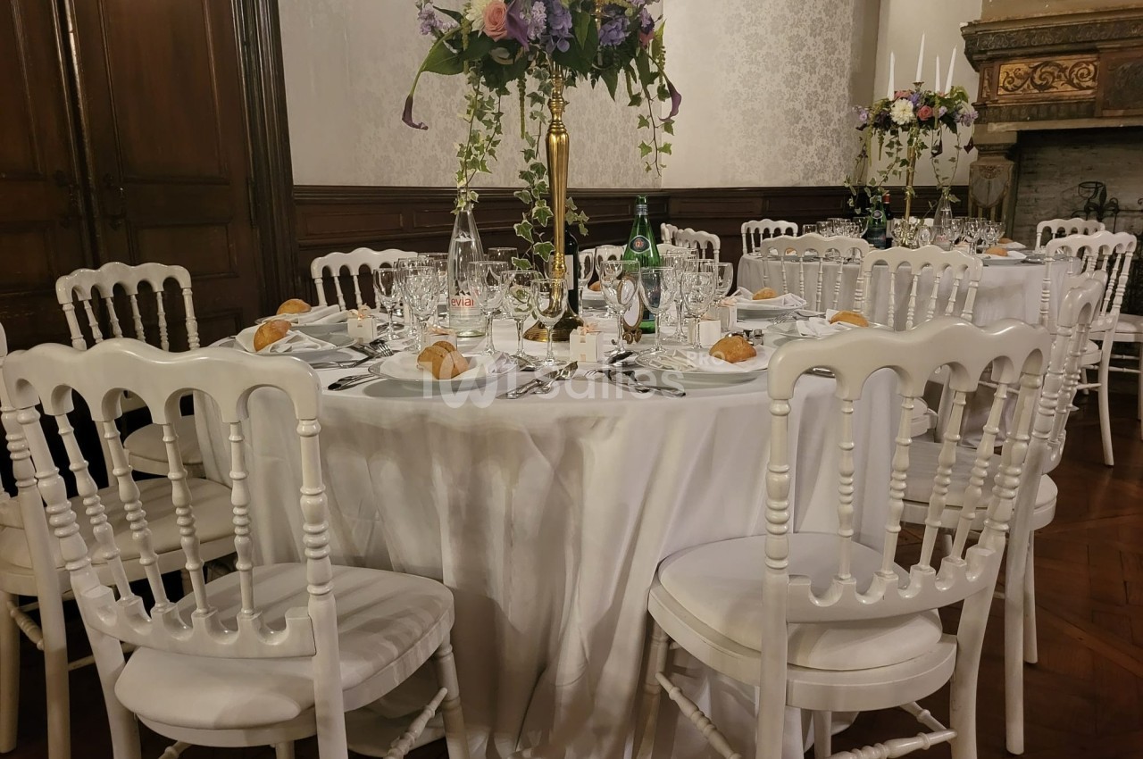 Table ronde élégamment dressée avec nappes blanches, chaises assorties, vaisselle raffinée et centre de table fleuri.