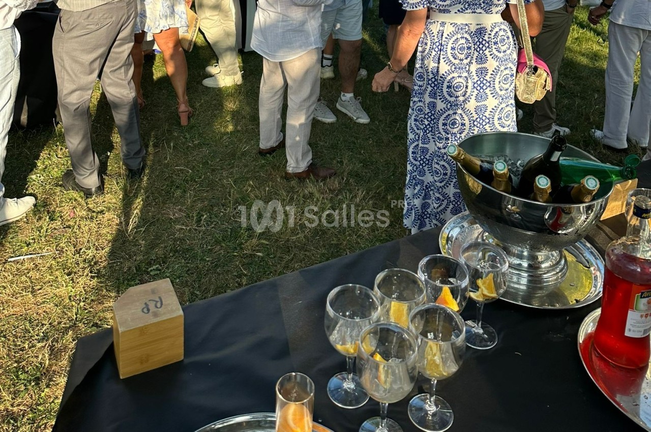 Personnes debout discutant dans un jardin, avec une table contenant des verres et un seau à champagne au premier plan.