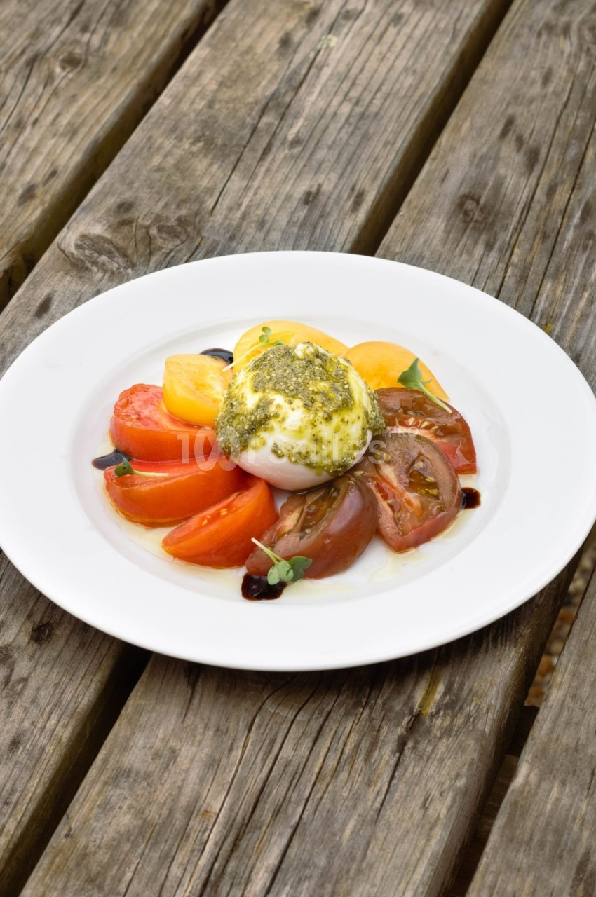 Assiette de burrata garnie de pesto, accompagnée de tomates colorées, posée sur une table en bois rustique.