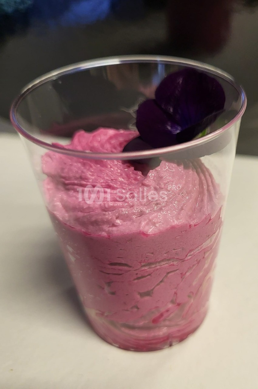 Mousse rose servie dans un verre transparent, décorée d'une fleur violette comestible.