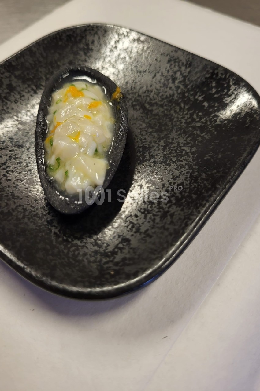 Une bouchée servie dans une coque noire, garnie de préparation crémeuse avec des touches de jaune et vert.