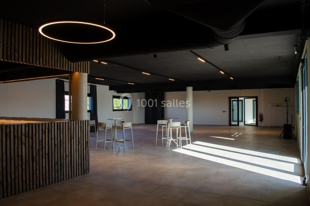 Salle spacieuse avec un sol en carrelage, des tables hautes, un éclairage moderne et de grandes fenêtres laissant entrer la…