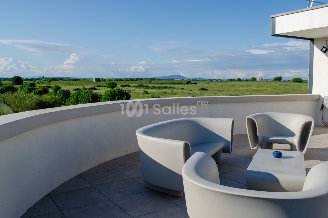 Mobilier de jardin moderne sur une terrasse arrondie avec vue sur une prairie et un ciel dégagé.