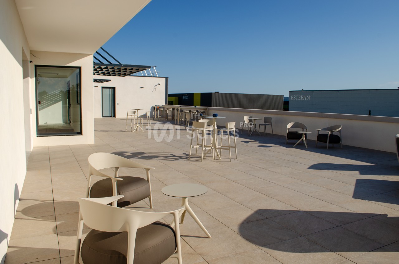 Terrasse spacieuse avec mobilier moderne, tables et chaises, sous un ciel dégagé en fin de journée.