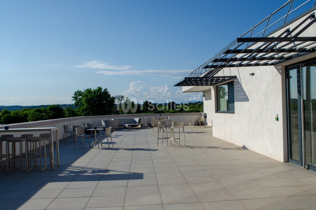 Grande terrasse ensoleillée avec mobilier minimaliste, vue sur un paysage verdoyant et ciel dégagé.