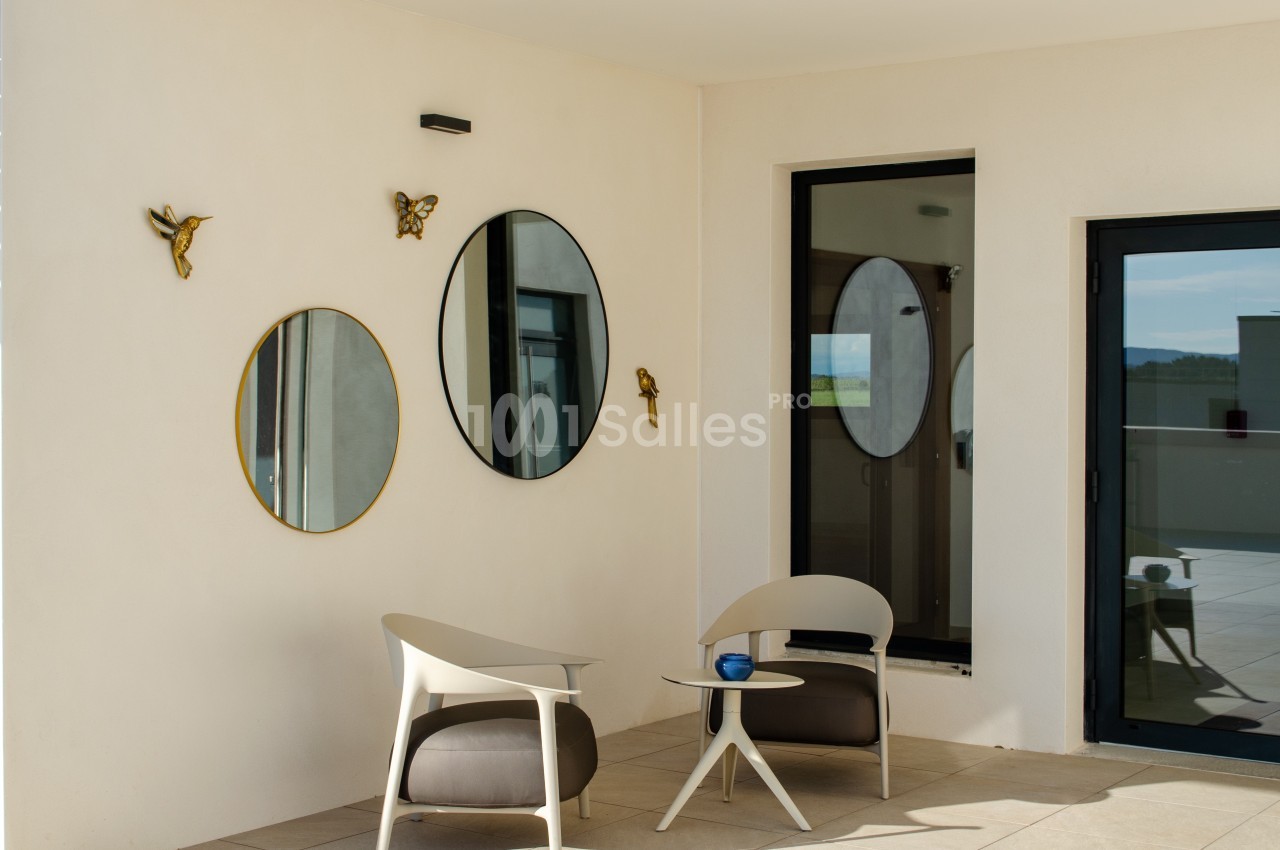 Deux fauteuils modernes et une table basse sur une terrasse, avec des miroirs ronds et des décorations murales.