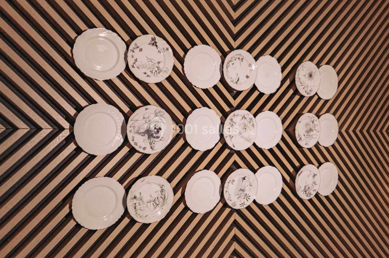 Assiettes blanches et décorées disposées en motif géométrique sur un mur à rayures diagonales.