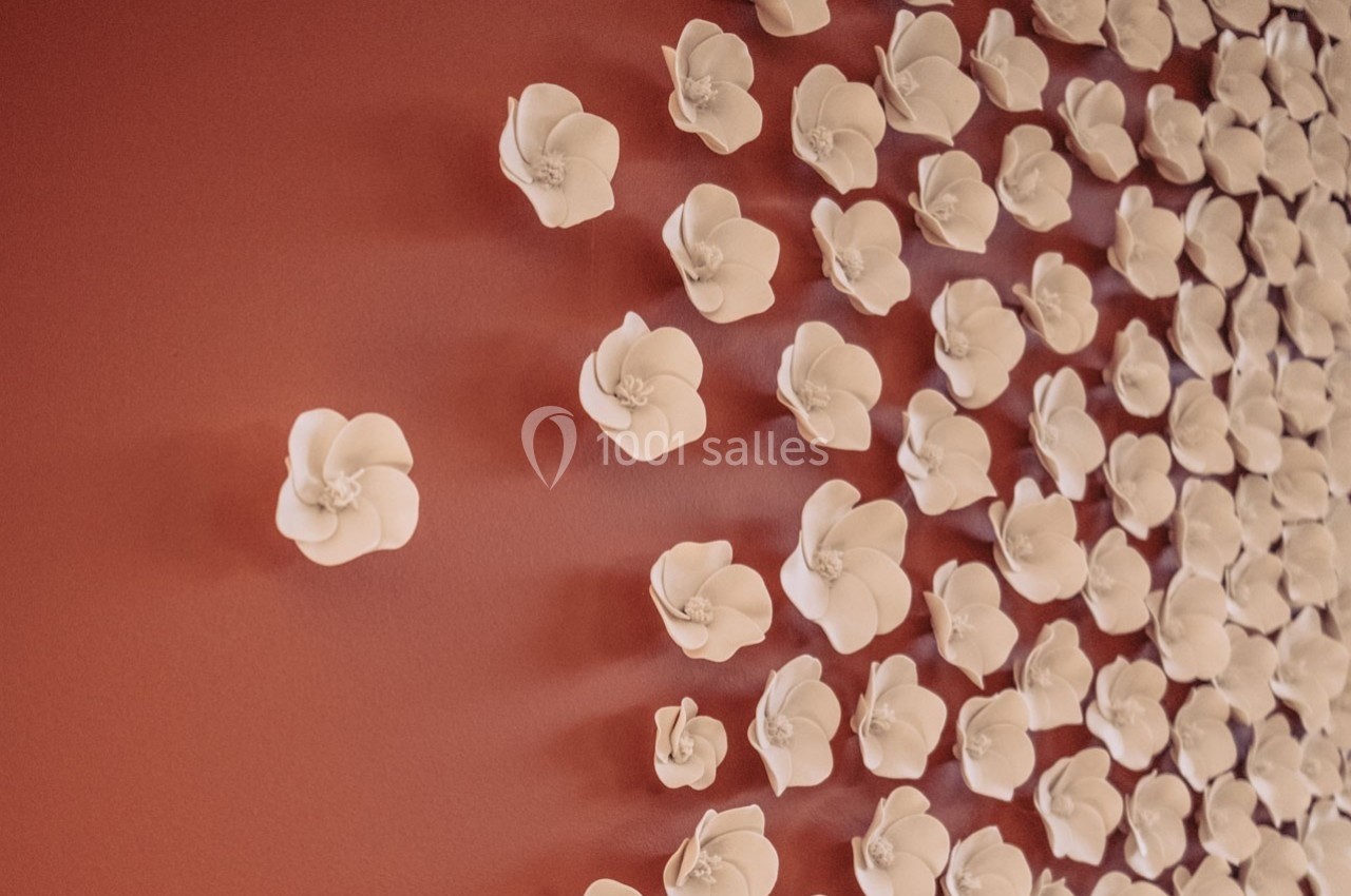Fleurs blanches en céramique fixées sur un mur rouge, formant une composition artistique.