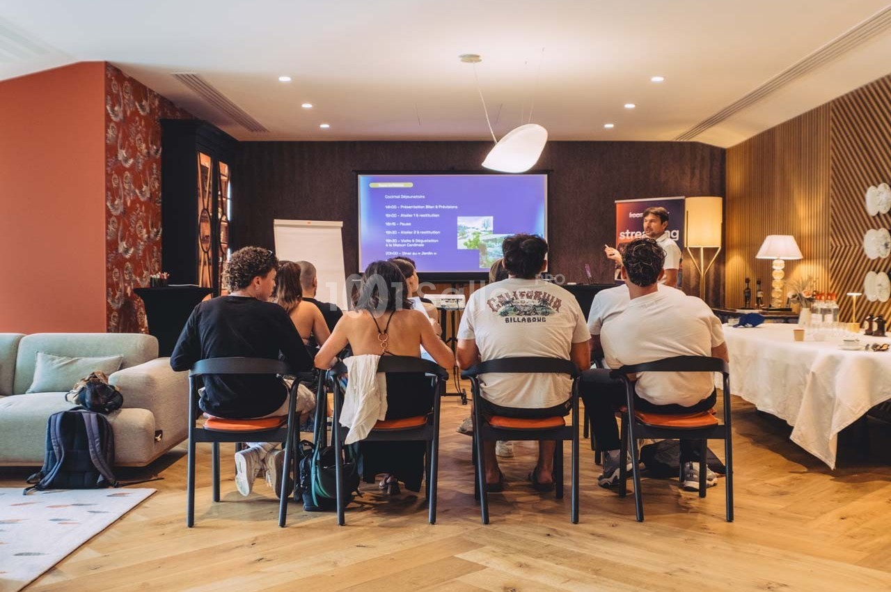 Des personnes assises assistent à une présentation projetée sur un écran dans une salle aménagée.