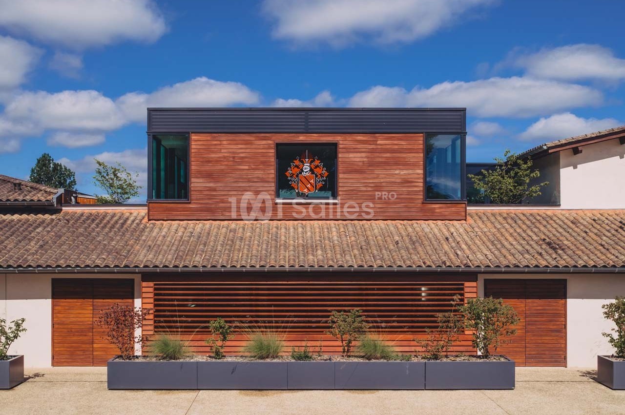 Façade d'un bâtiment moderne en bois avec un étage vitré et des plantes alignées devant.