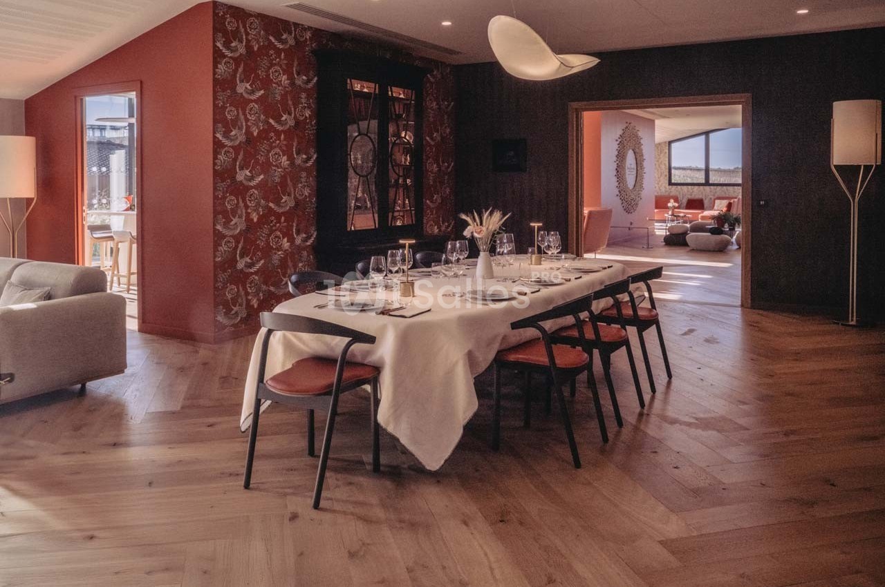 Salle à manger élégante avec une grande table dressée, éclairée par une lumière naturelle et entourée d'un décor chaleureux.