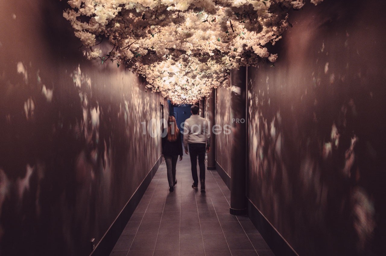 Un couple marche dans un couloir sombre décoré de fleurs blanches suspendues au plafond.